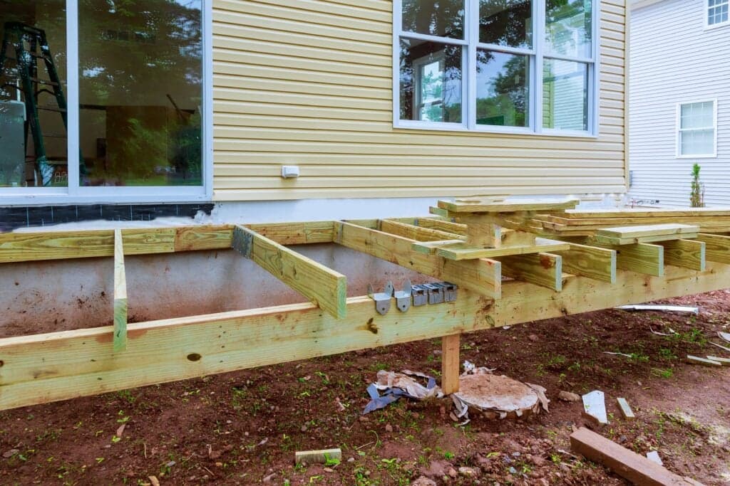 Professional deck framing installation in Ocala, Florida, featuring pressure-treated wood joists and metal hangers attached to a suburban home exterior.